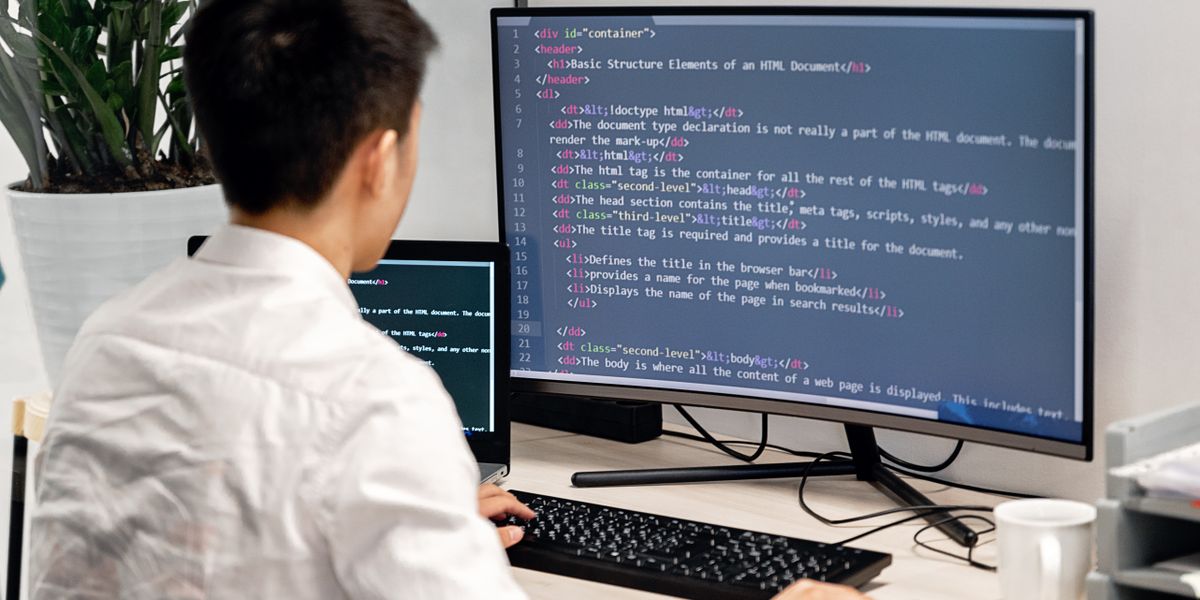 後ろ姿でモニターにHTMLコードを表示しながら作業するエンジニア